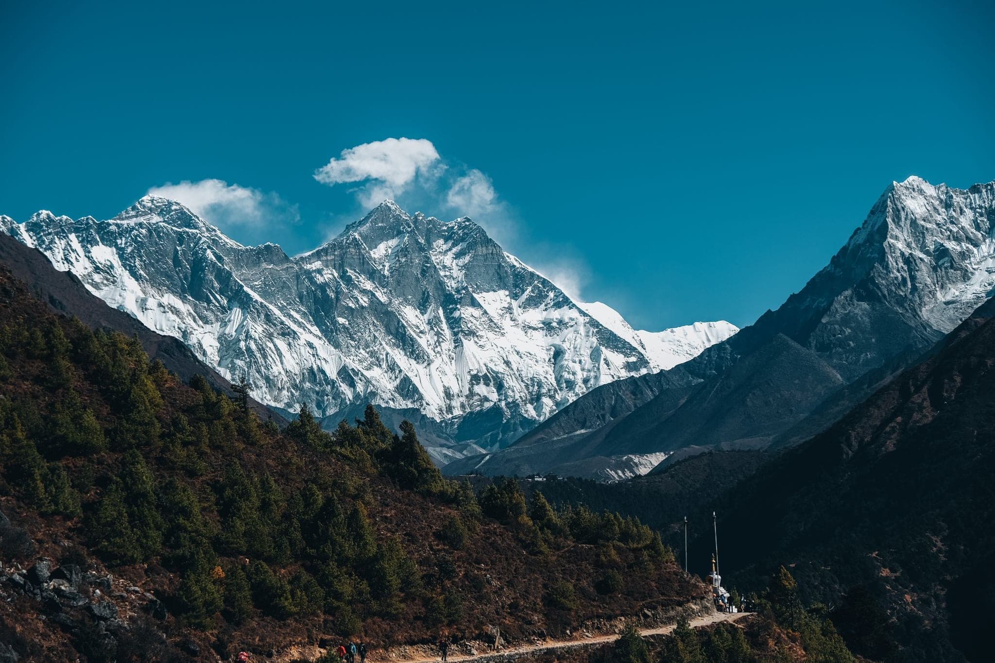 Trekkers on a hillside trail below Everest and the great snow wall of Lhotse
